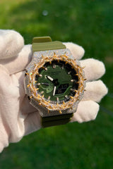 A custom green watch with a diamond-encrusted bezel and spiked details, held by a hand wearing a white glove against a blurred green grass background.